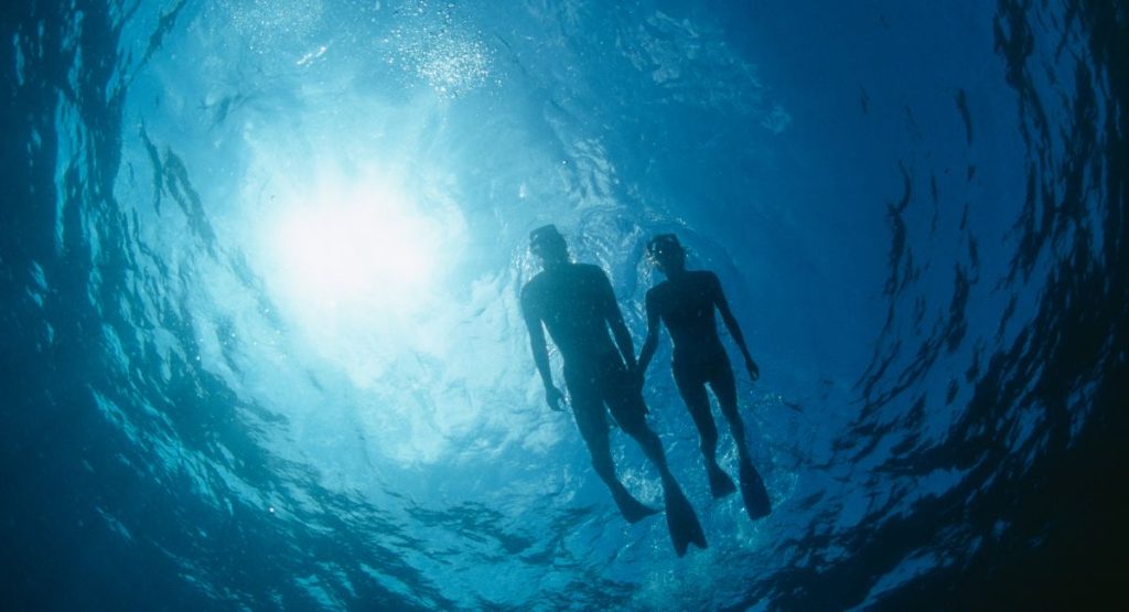 Silhouette of male and female snorkeling in dark water with sun shining through surface. snorkeling san diego.