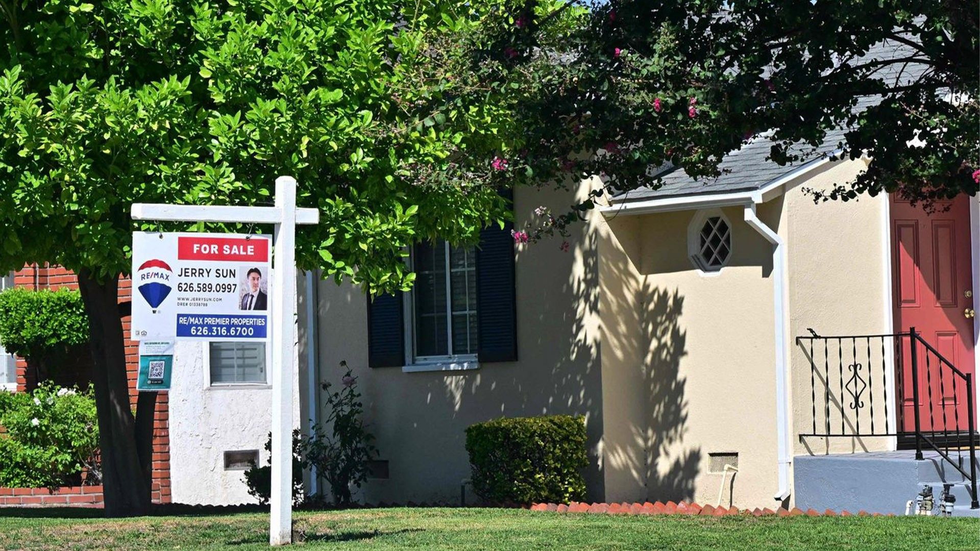 A 'for sale' sign posted on the lawn in front of a single-family home