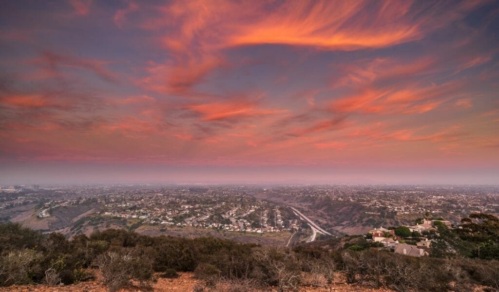 Views from Mount Soledad over La Jolla suburbs during sunset with pink/orange clouds on a purple sky