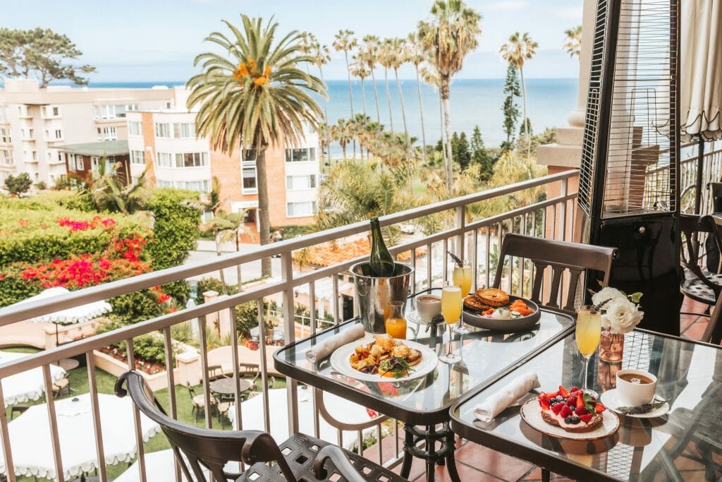 Table set with brunch items, mimosas and champagne on a balcony overlooking the ocean at La Valencia hotel in La Jolla