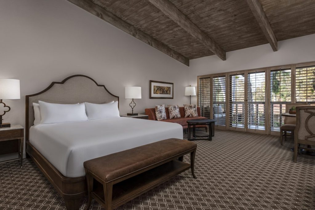 Hotel room with large king size bed with all white sheets, couch and seating area, with wooden vaulted ceilings and outdoor patio. Rancho Bernardo Inn, Boutique Hotels San Diego.