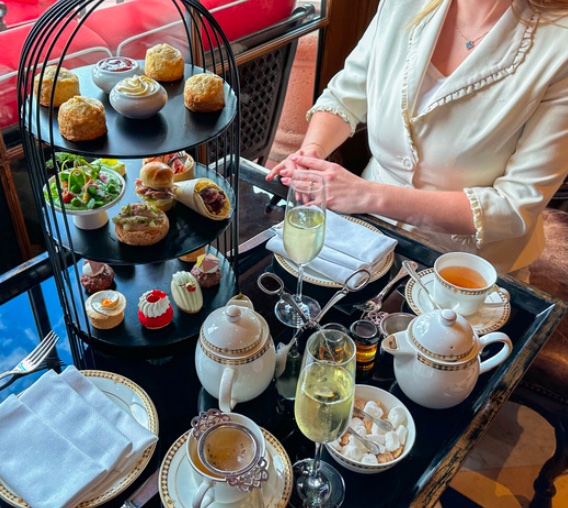 shot from top: person sitting on table with afternoon tea delicacie like pastries, cakes, sandwiches, tea and champagne.