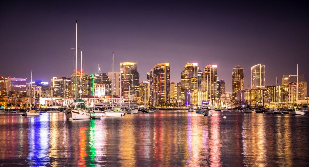 City skyline reflecting on water at night, boats sit on the colorful bay. San Diego skyline at night, Things to do in San Diego in November.