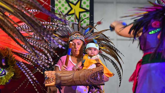 A drummer holding her grandson performs with The Mexi'cayotl Indio Culture Center Aztec dancers at the 2019 National Latino Family Expo.