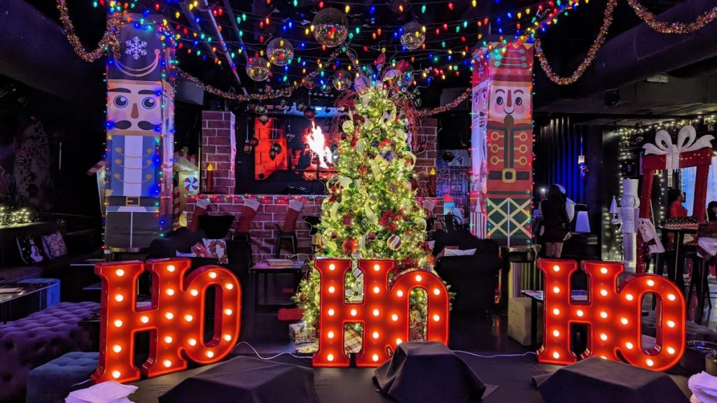 Inside of Santa's Lair Night Club with red lettering "Ho Ho Ho" and Christmas tree and decoration behind it