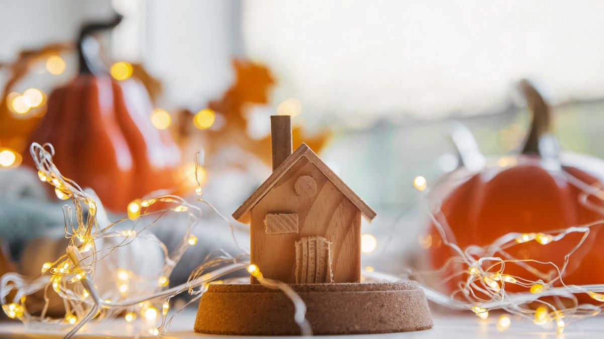 White decor pumpkin and house model on background of textured light sweaters in defocus