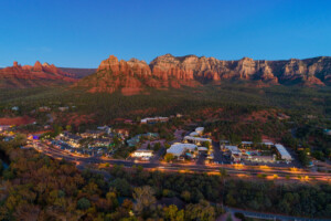 Sedona Verde Valley aerial at dusk during autumn, with mountains in the background and a highway with stores and forests in the foreground.