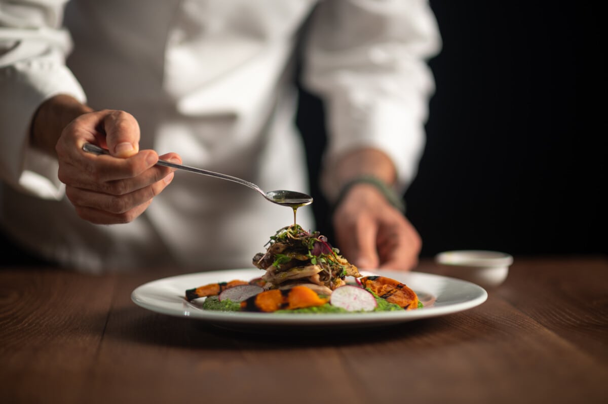 A chef pouring sauce from the spoon on meal on a black background.