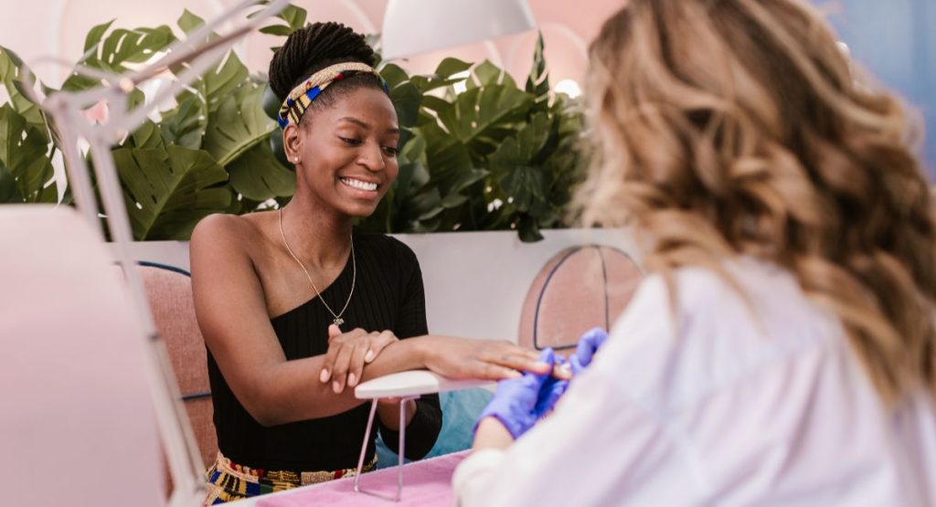 Woman smiling while having a manicure at a cute spa with pink decor and green plants. Spas in San Diego.