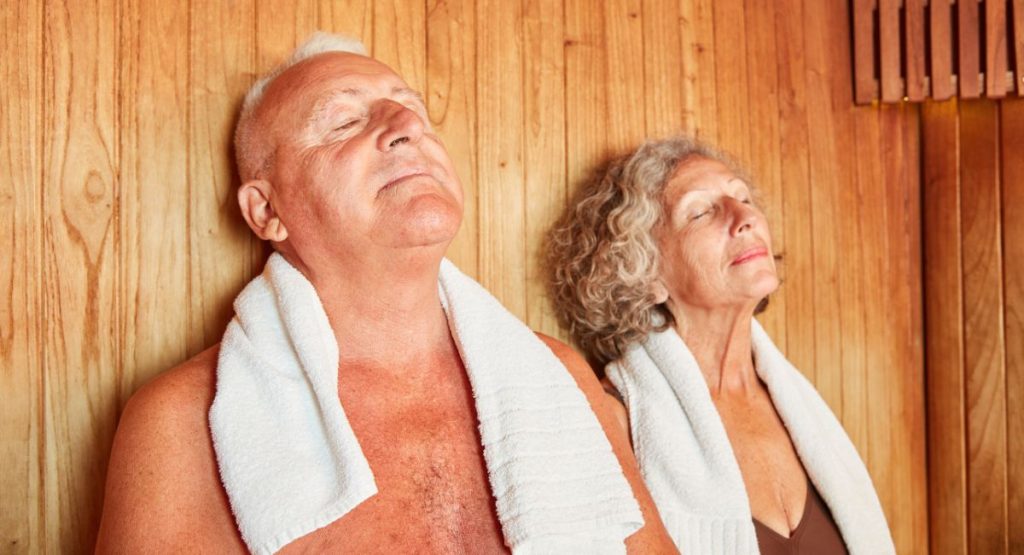 Older man and woman relaxing in wooden sauna with towels around their necks.San Diego Spa Resort.