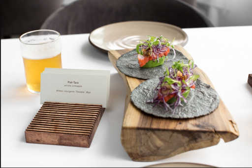 Two small fish tacos on a wood plank at a table