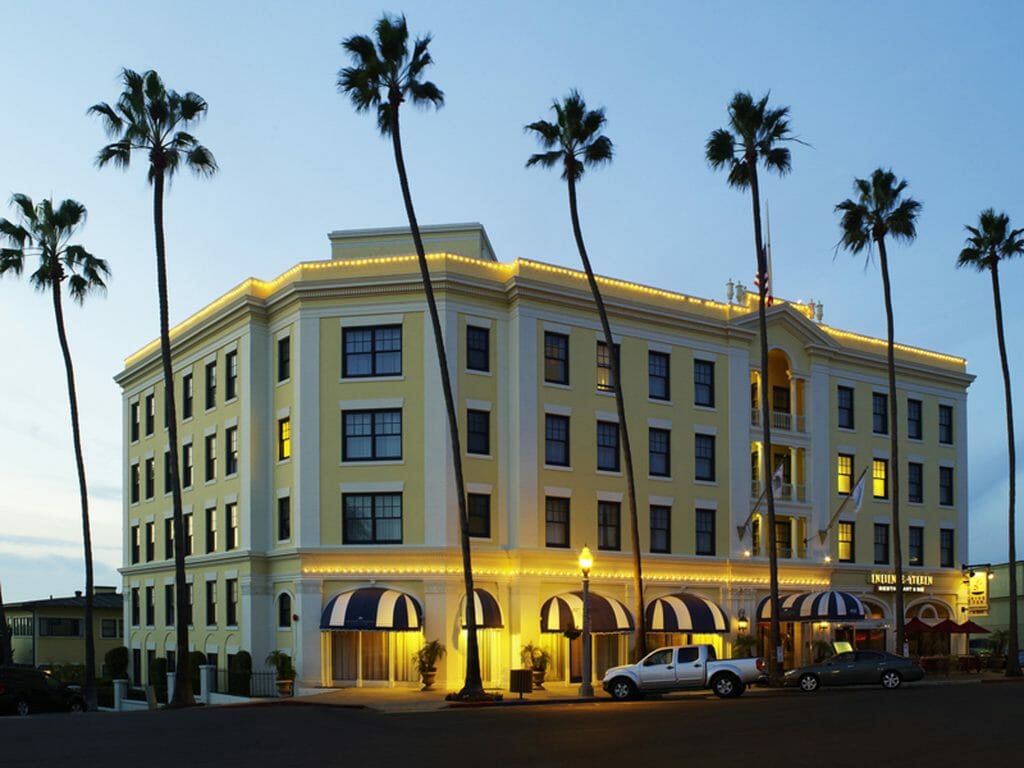 Exterior Photo of Grande Colonial Hotel La Jolla - a 4 story yellow corner building surrounded by palm trees