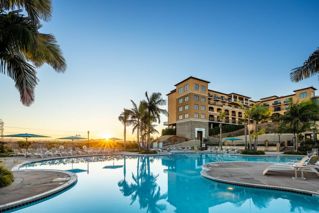 View over rounded pool with the sun breaking over the horizon and the yellow Mediterranean style hotel building to the right