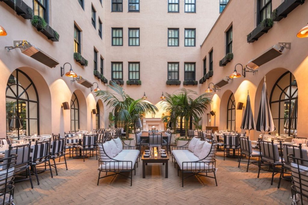 Spacious courtyard with outdoor tables and dining areas and plants, with brick floor under Spanish-style building, The Guild Hotel, Boutique Hotels San Diego.