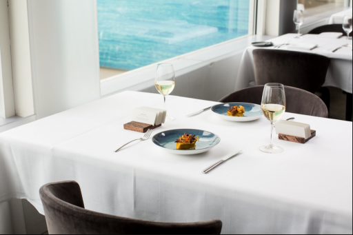 A beautiful white tableclothed table is adorned with plates of food while outlooking on the beach