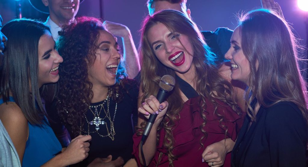 Group of people smiling and singing at karaoke in a bar.