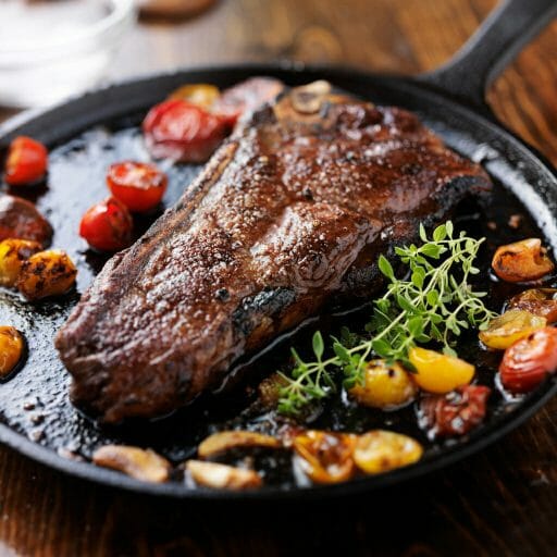 new york strip steak on iron skillet with heirloom tomatoes