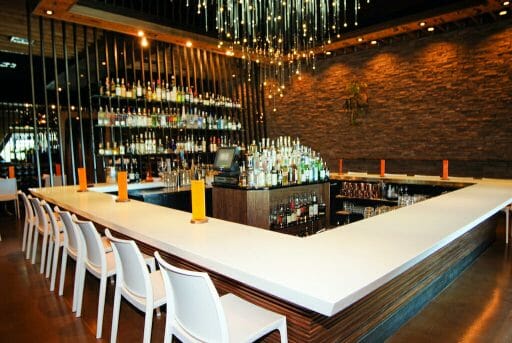 A sparkling chandelier hangs above an open bar area, chairs empty but the threads of a party still lives. the liquor is neatly placed on the back wall for guests to choose from