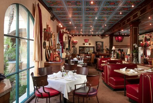 A dining room filled with warm colors like red on lovely wood floors brightly lit by natural light