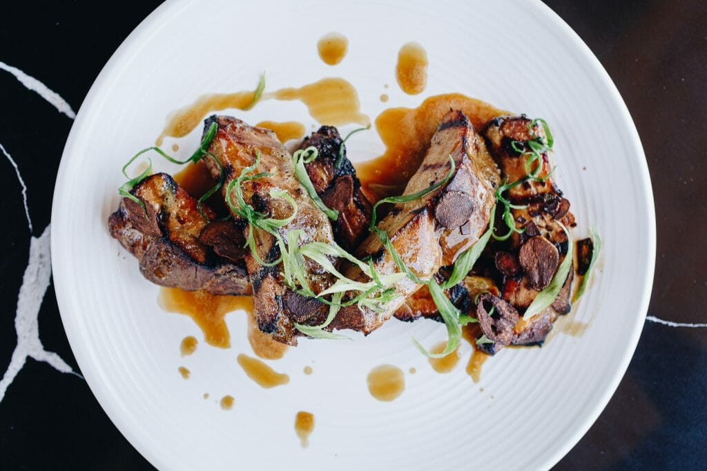 Several ribs are lovingly placed on the white plate then sauced over and garnished with greenery