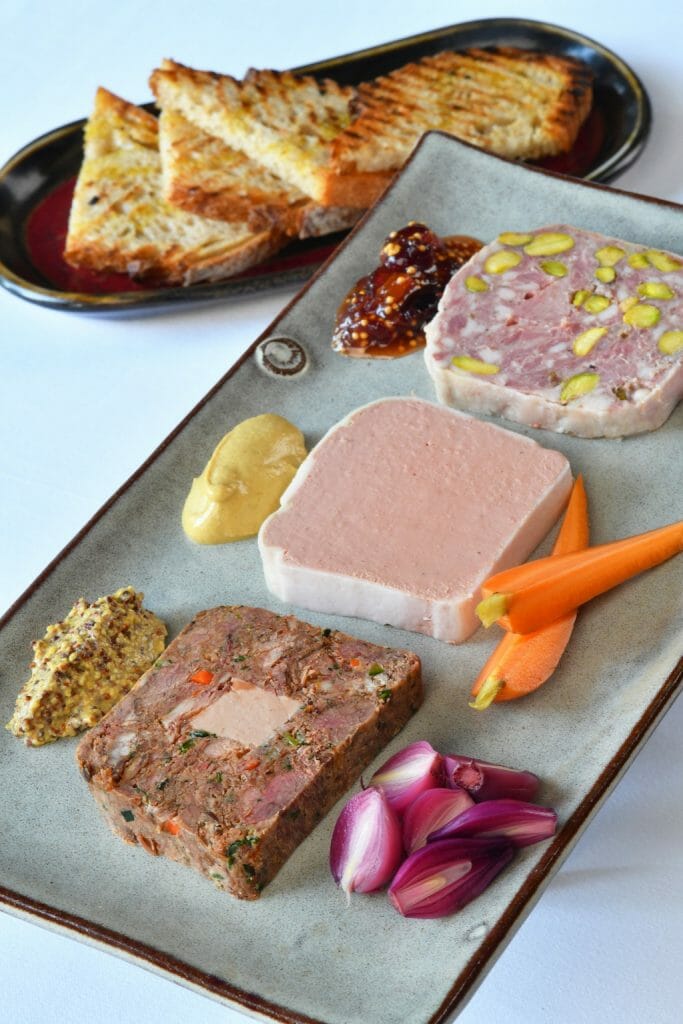 Three different pates lined up on a white plate with edible garnishes