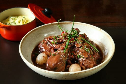 Classic coq au vin with a pot of mashed potatoes behind it