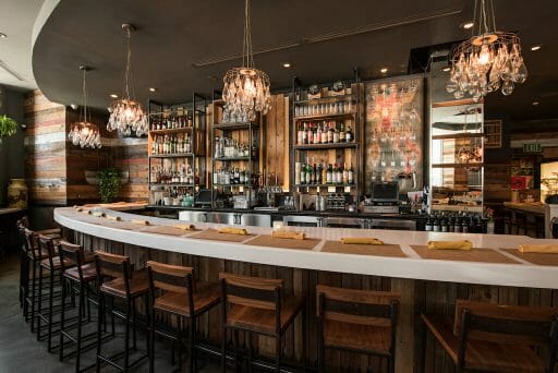 Natural wood bar with selves filled with prime alcohol lit by humble chandeliers