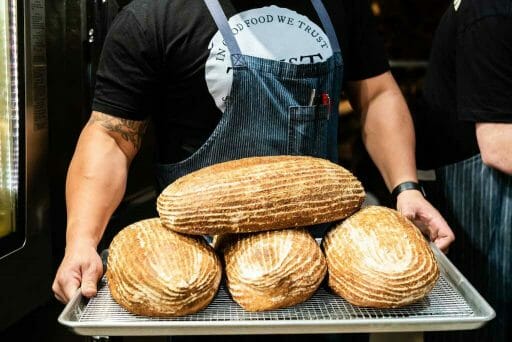 Incredible burly man carrying a beautiful tray of sourdough bread loaves