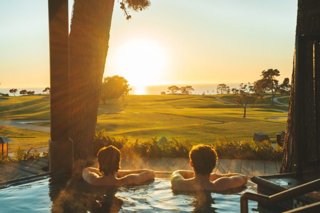 Couple in outdoor jacuzzi watching sunset over golf course and ocean in the distance. The Lodge at Torrey Pines Best hotels in San Diego for Couples