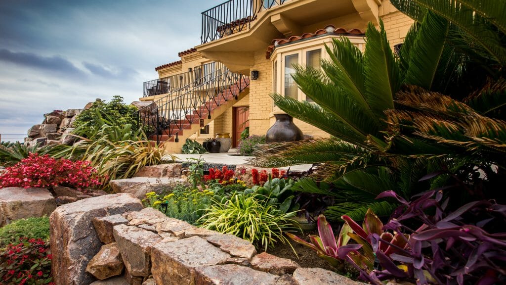 Lush garden beds with flowers and palm trees in front of yellow luxury hotel in La Jolla Pantai Inn