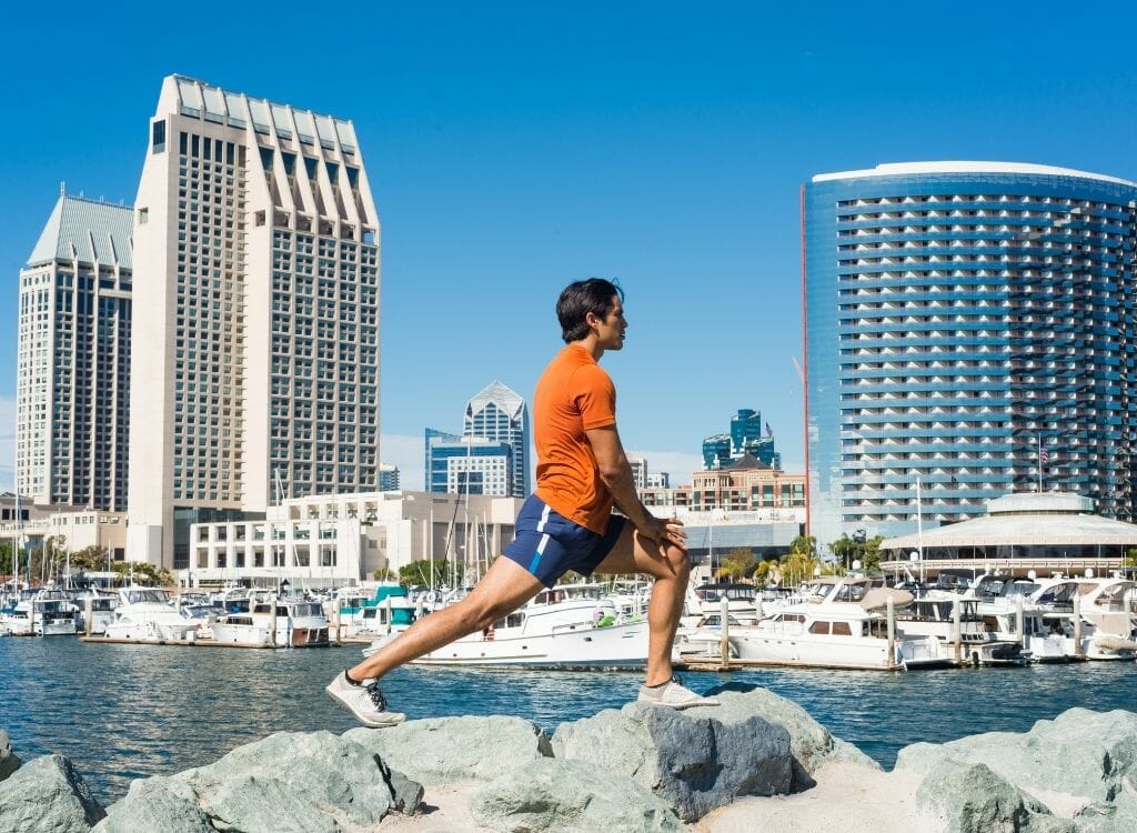 Male runner stretching on rocks in front of San Diego Skyline