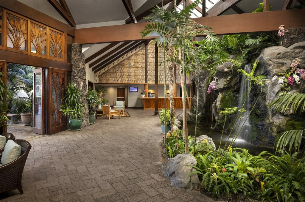 Catamaran Resort Lobby with lush plants and waterfall on the right and tropical/polynesian decor and architecture on the left