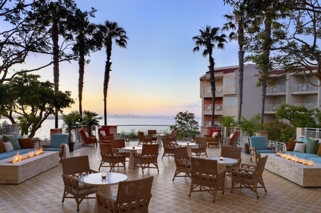 Outdoor courtyard with large seating area and fire places surrounded by hotel building and palm trees, courtyard looks out over ocean views during sunset. Loews Coronado Bay Resort, Romantic Hotels in San Diego