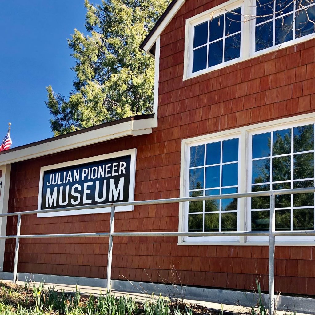 Red wood building with white trim and a black sign with white letters: Julian Pioneer Museum