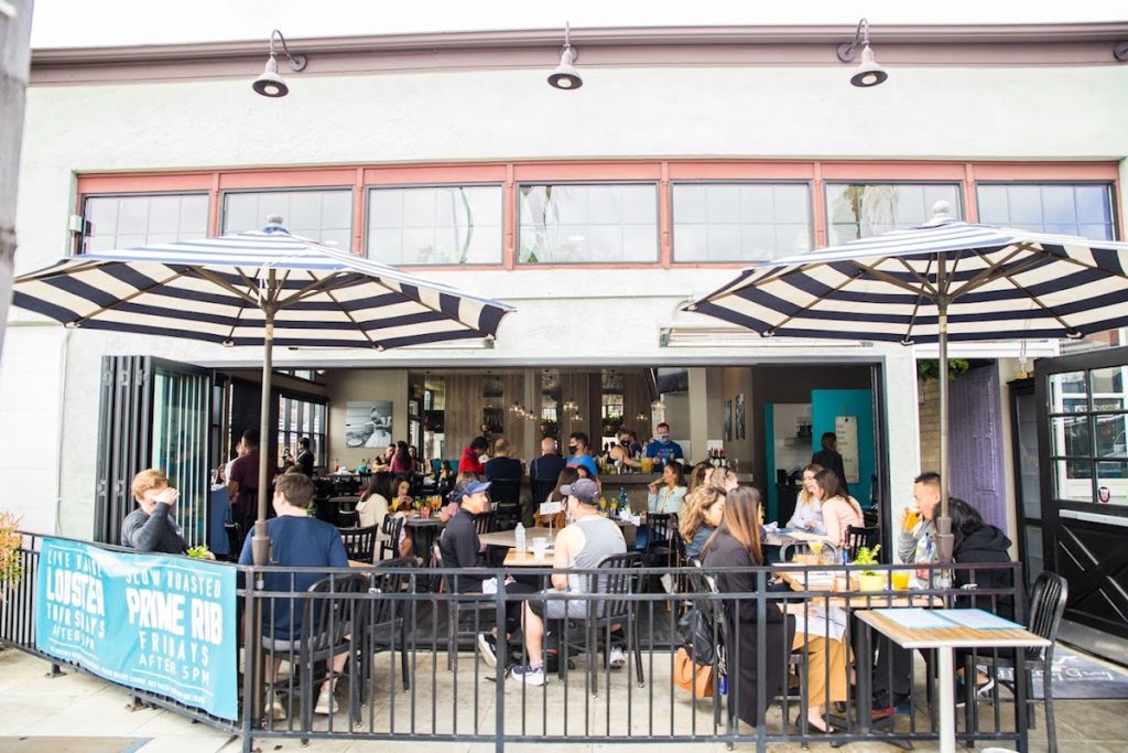 People sitting at table under outdoor patio, which opens to restaurant interior space. Harley Gray Kitchen & Bar.