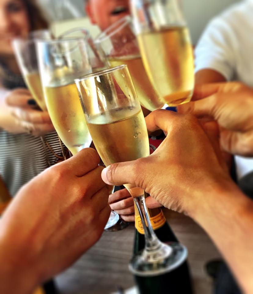 Group of people cheers-ing with Champagne in Champagne flutes. Harley Gray Kitchen & Bar, Bottomless mimosas in San Diego.