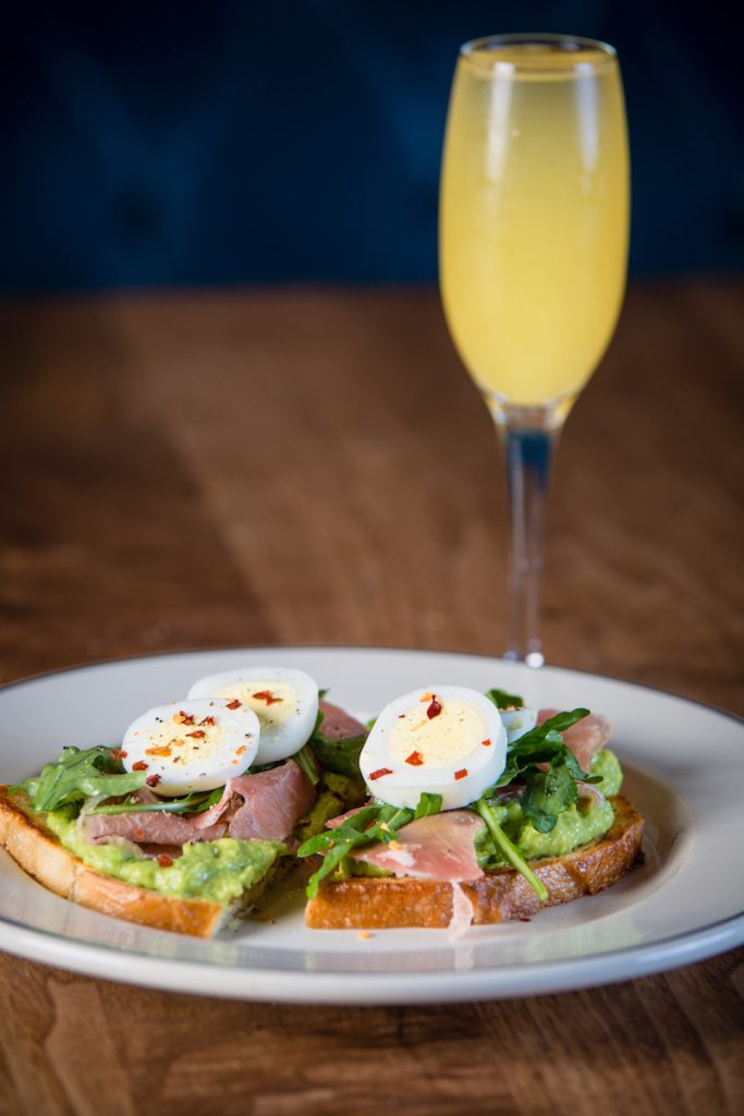 Avocado toast with ham and eggs, mimosa in background. JImmy's Famous American Tavern, Bottomless Mimosa Brunch San Diego