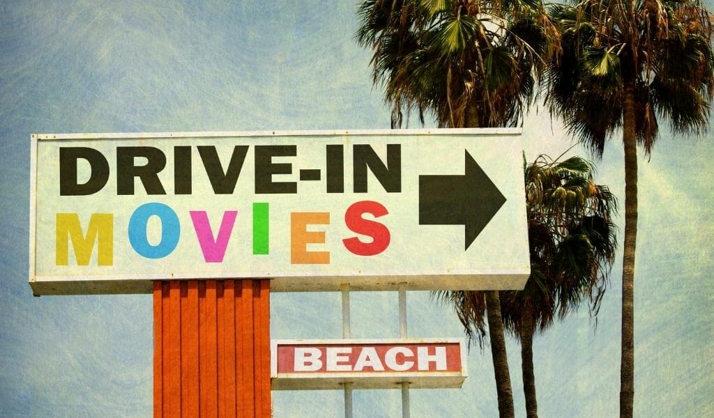 Vintage style photo of a sign for drive in movie theater at the beach and palm trees behind it. 