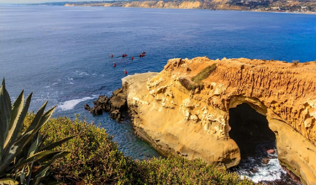 Sand stone cliffs in La Jolla cove with kayakers paddling in the background