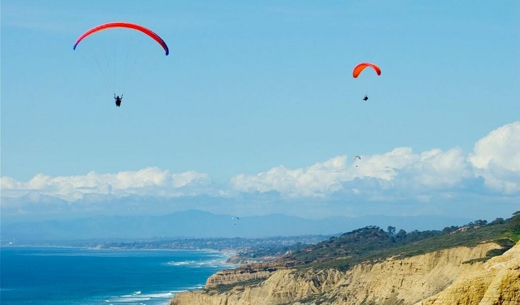 Two Cliff Gliders with parachutes gliding over the ocean cliffs in La Jolla - Romantic Things to do in San Diego