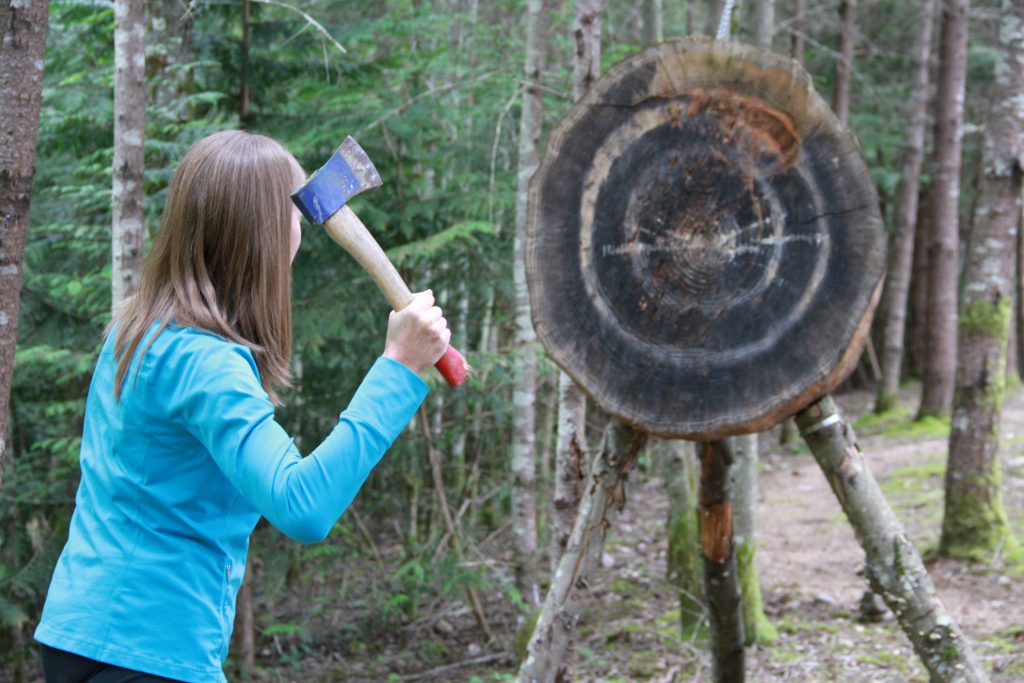 Woman in blue shirt in the forest throwing an axe towards a wood target