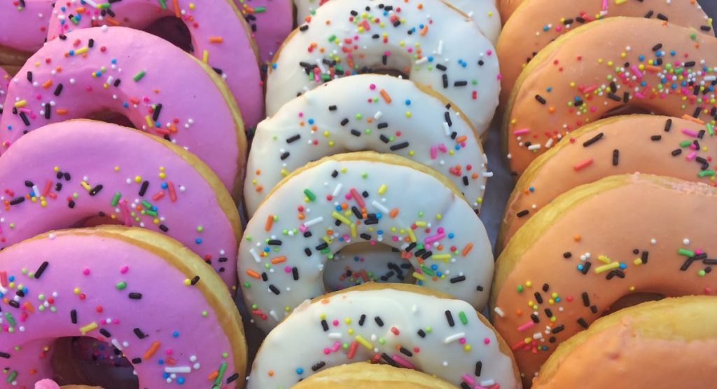 Close up of pink, white, and orange frosting-covered donuts with sprinkles.