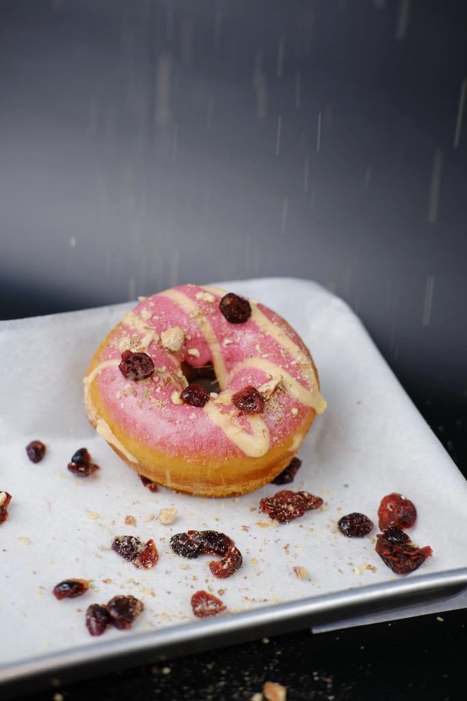 Close up of cranberry flavored donut with pink frosting. Nomad Donuts, where to get the best donuts in san diego