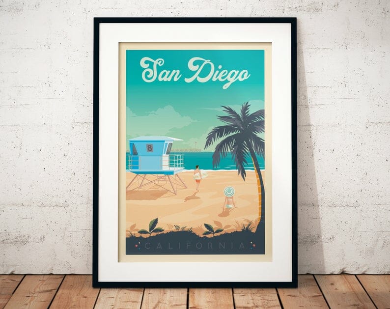 vintage print of San Diego coast line picturing beach, ocean, palm tree, and lifeguard tower and turquoise ocean, leaning on a white wall