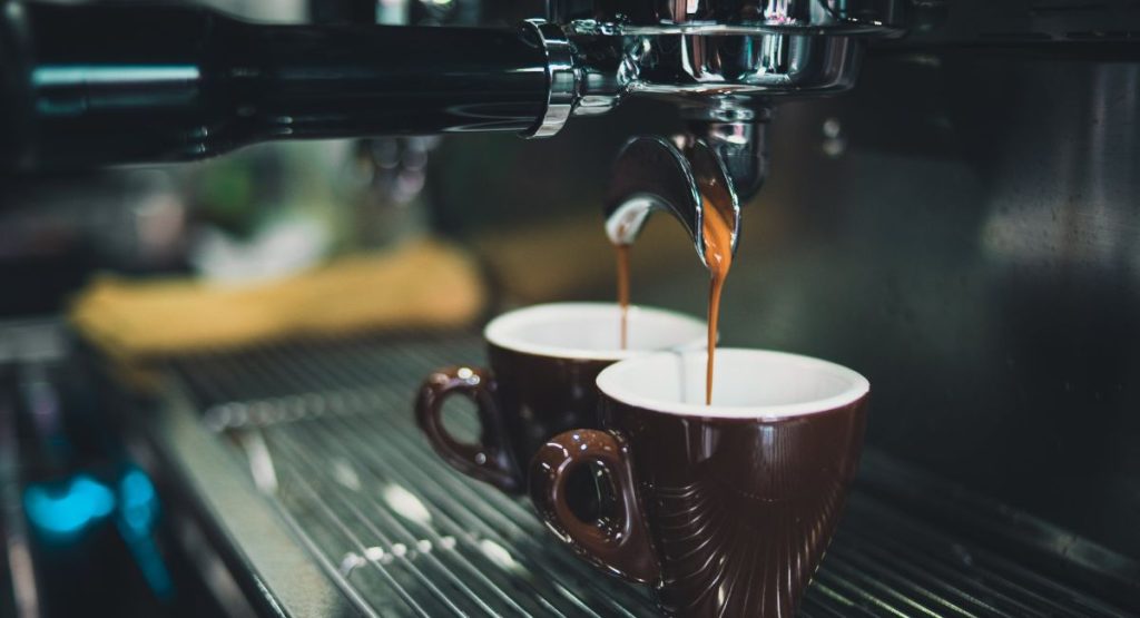 Espresso machine pouring espresso into two brown coffee mugs.