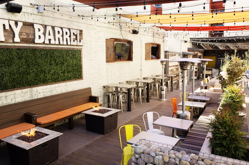 Restaurant dining area with relaxed seating, fire pits, string lights, and large sign reading "knotty barrel". Knotty Barrel, sports bars San Diego.