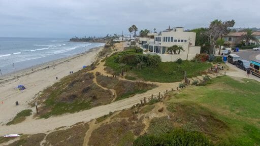 The water crashes onto the La Jolla shore as people idly walk across the beach and the buildings overlook the beautiful horizon