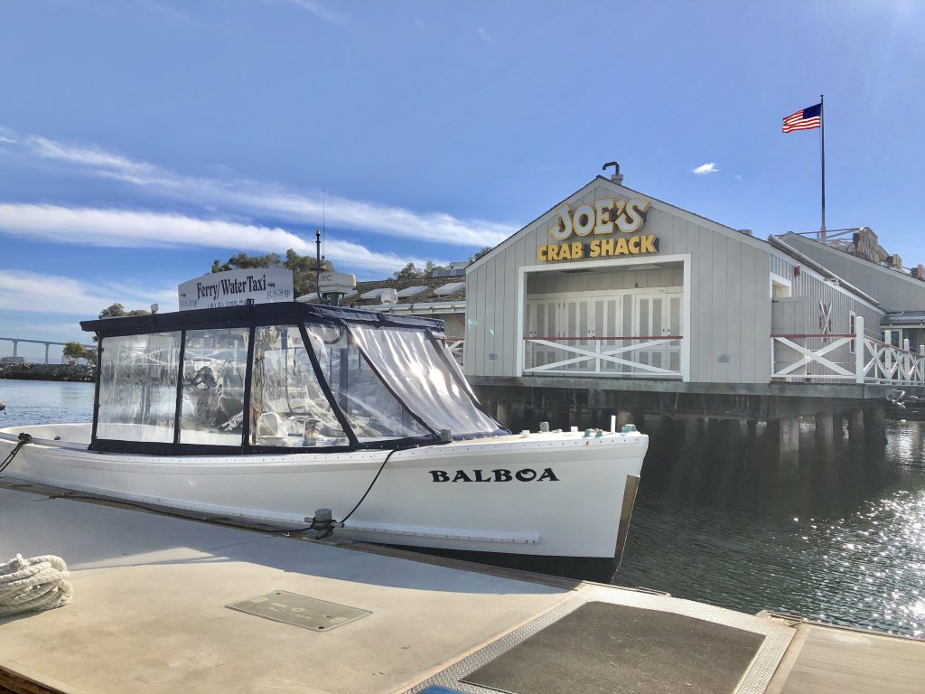 San Diego Coronado Ferry Small white boat called Balboa tied up on pier with Joe's Crab Shack Restaurant in the background in San Diego