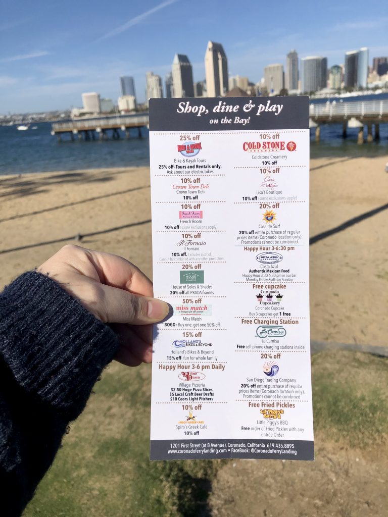 Free Discount card for shops and restaurants at Coronado Ferry Landing held up in front of San Diego Skyline