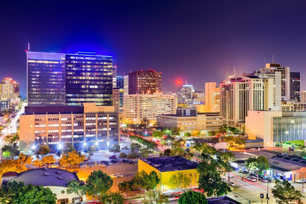 Lights from the towering buildings glow in the night at the streets buzz with light and activity in downtown San Diego